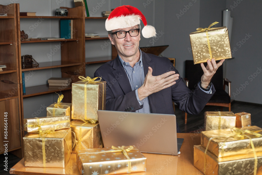 Happy Christmas businessman wearing Santa hat showing gold gift box in office