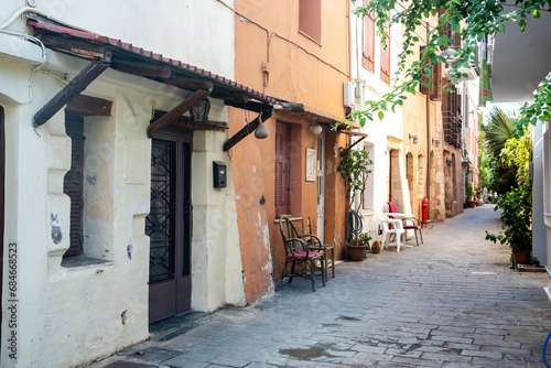 Crete island Greece, Chania Old Town. Table, chair out of building and potted plant on paved alley.