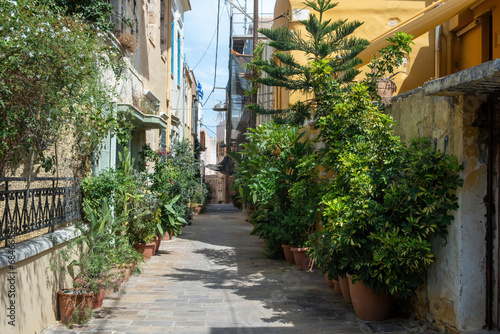 Paved alley surrounded with potted plant between building. Chania Old Town, Crete island, Greece.