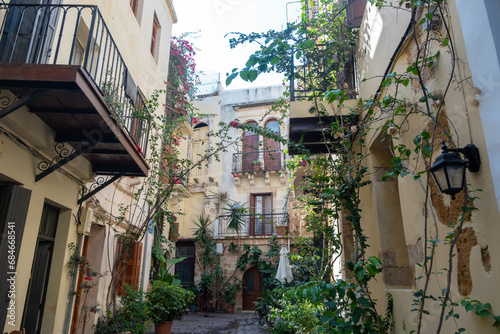 Fototapeta Naklejka Na Ścianę i Meble -  Pot with plant on paved alley, building, balcony, summer day. Greece Crete island, Chania Old Town.