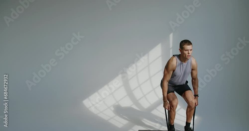 Young athletic man has workout and doing deadlift exercise using resistance band in studio with white background. Guy with muscular body exercising with sport equipment. photo