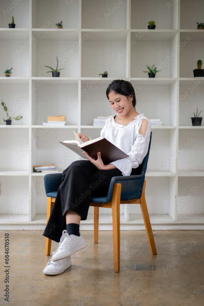 Full size portrait of Asian woman sitting and reading a book in the break room. Relaxation corner at work Full size portrait of Asian woman sitting and reading a book in the break room. Relaxation corner at work