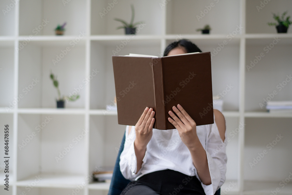 A picture of a woman sitting and reading with a book covering her face. - obrazy, fototapety, plakaty 