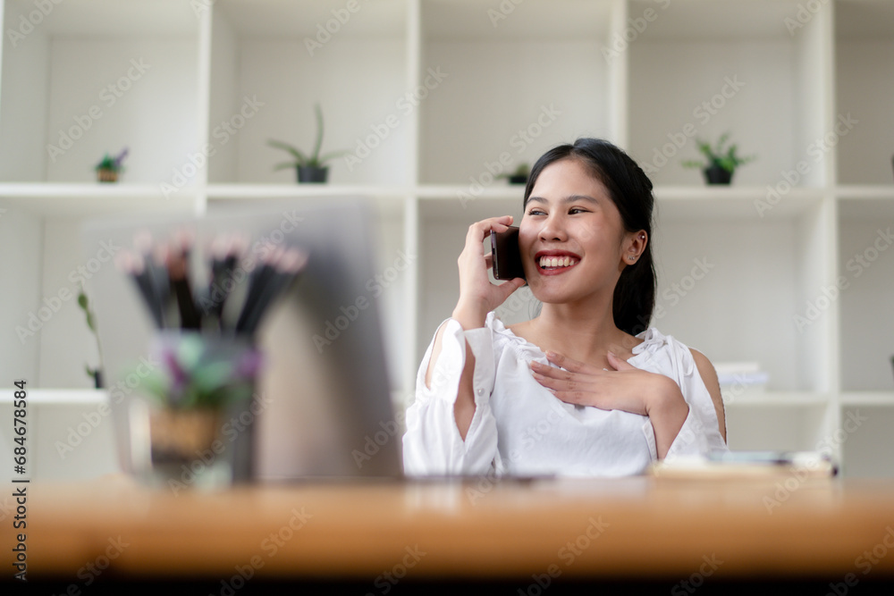 Happy Asian woman talking on the phone while sitting in the office. Happy Asian woman talking on the phone while sitting in the office.