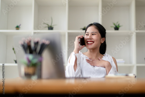 Happy Asian woman talking on the phone while sitting in the office.