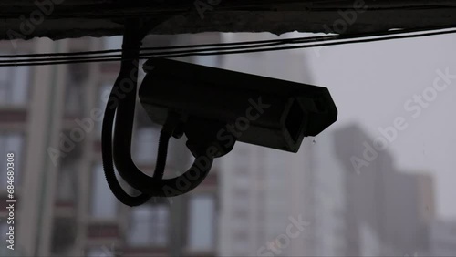 Heavy rain falls in slow motion behind silhouetted security camera