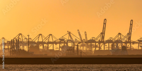 Dutch industrial area with shipping cranes during sunset in Europoort, Rotterdam harbor photo