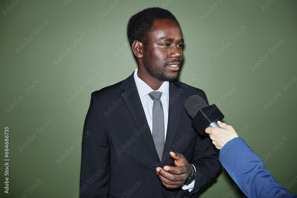Medium shot of cheery Black man in business suit giving answers to interviewer
