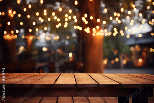 An empty wooden table with a soft focus on the festive blurred bokeh lights hanging from the trees in the background. Cozy evening at cafe concept