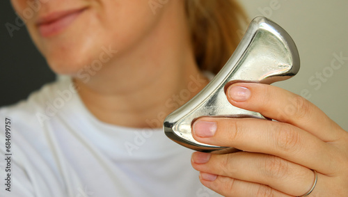 Young caucasian woman smiling and holding a metal gua she tool for lifting the face photo