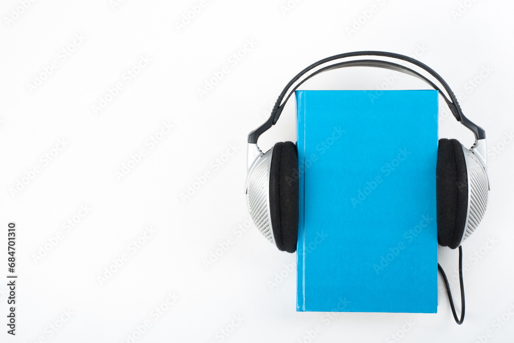 Audiobook on white background. Headphones put over blue hardback book, empty cover, copy space for ad text. Distance education, e-learning concept. Top view Audiobook on white background. Headphones put over blue hardback book, empty cover, copy space for ad text. Distance education, e-learning concept. Top view