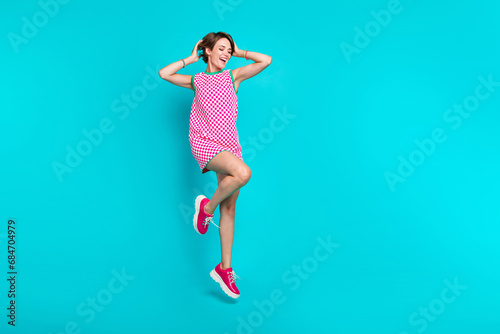 Fototapeta Naklejka Na Ścianę i Meble -  Advertisement banner image of young girl full body cadre jump touching her bob brown hairstyle lightness isolated on cyan color background