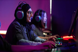 Side view portrait of Muslim young woman playing video games in cybersports club and smiling happily, copy space