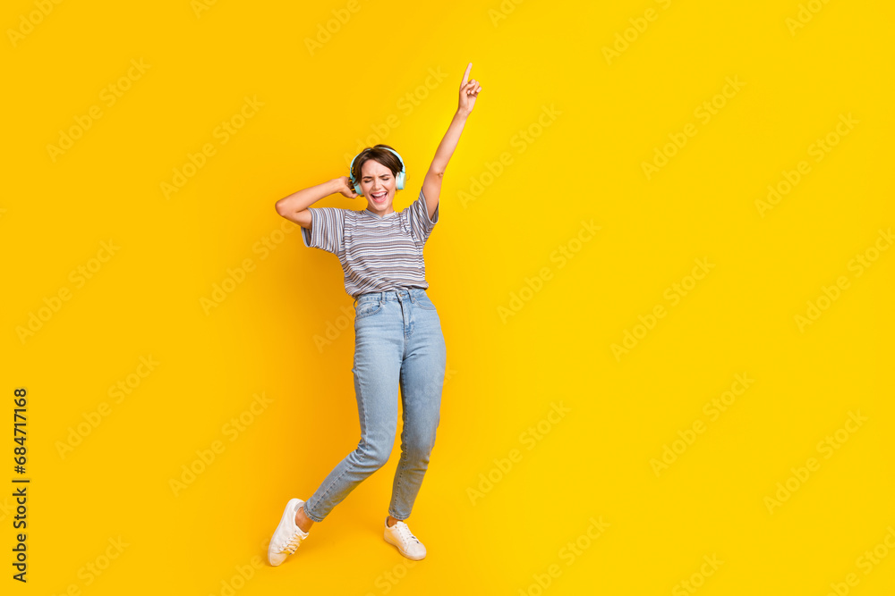 Full length portrait of crazy person touch headphones point finger rejoice empty space isolated on yellow color background