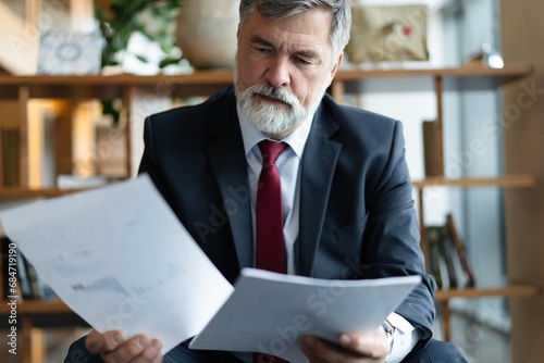 Mature businessman in formal suit concentrating on reading the report, sitting in the lobby and preparing for the meeting. photo