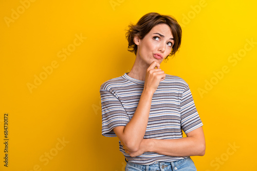 Portrait of suspicious girl with short hairdo wear grey t-shirt hold finger on chin look empty space isolated on yellow color background
