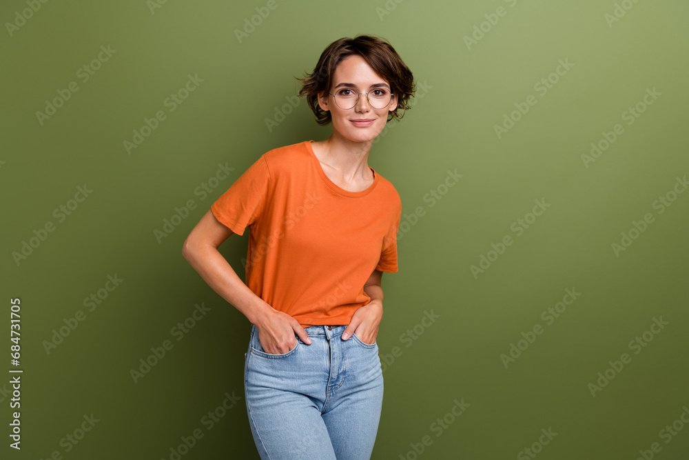 Photo of clever adorable cheerful girl with bob hairdo dressed orange t-shirt hold palms in pockets isolated on khaki color background Photo of clever adorable cheerful girl with bob hairdo dressed orange t-shirt hold palms in pockets isolated on khaki color background
