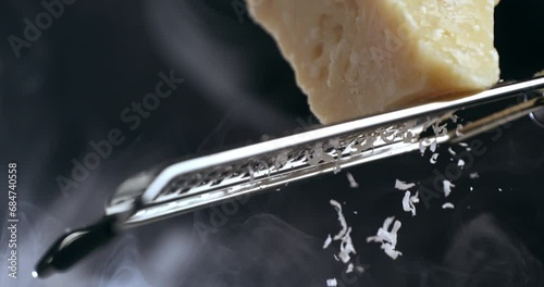 Super slow motion macro of a professional chef grating traditional parmesan cheese with steel grater on the dish close up and pieces of cheese fall at 1000 fps for preparing pasta. photo