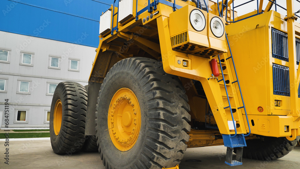 A large dump truck without a body. A huge dump truck standing near the factory walls. A yellow dump truck. Close-up. A large dump truck without a body. A huge dump truck standing near the factory walls. A yellow dump truck. Close-up.