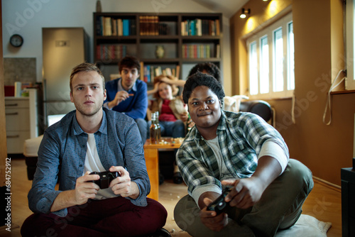 Friends playing video games together, group of young people with game controllers, multiethnic gamers on couch, casual gaming session, fun time at home photo