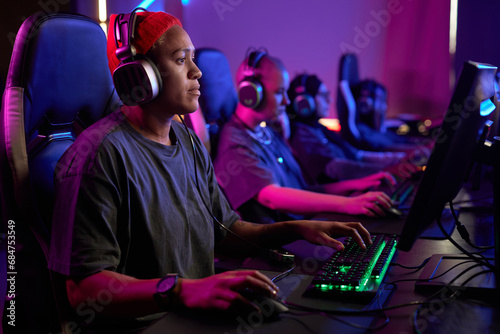 Side view portrait of Black woman playing video games professionally in cybersports club with neon lighting, copy space