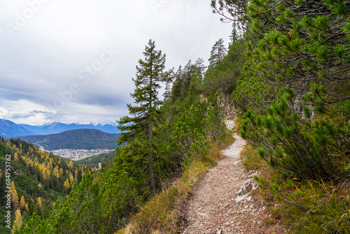 small path on top of a mountain with view towards alpine summits and cloudy sky 