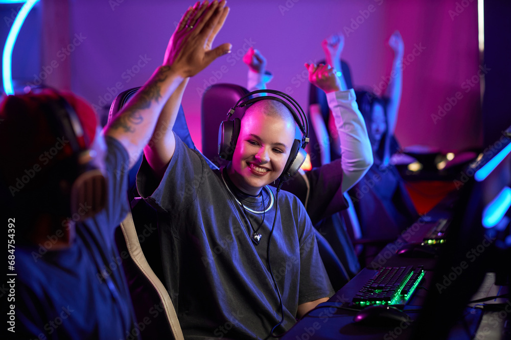 Obraz premium Portrait of smiling young woman in professional gaming tournament high five teammate and celebrating victory, copy space