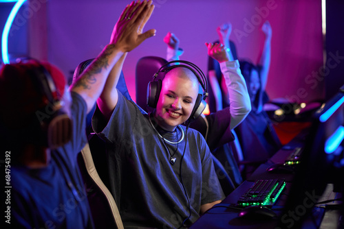 Portrait of smiling young woman in professional gaming tournament high five teammate and celebrating victory, copy space