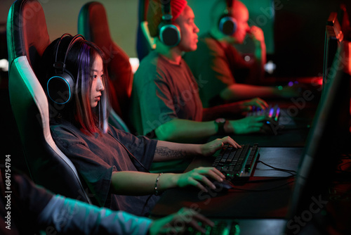 Side view portrait of young Asian woman playing video games in cybersports club and wearing pro headphones  copy space