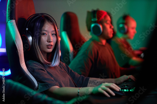 Portrait of tattooed young Asian woman playing video games professionally and looking at camera in neon light, copy space photo