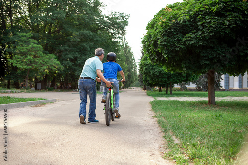 asian dad teaches son to ride bike, korean senior helps child, boy in helmet is actively relaxing with his father © Богдан Маліцький