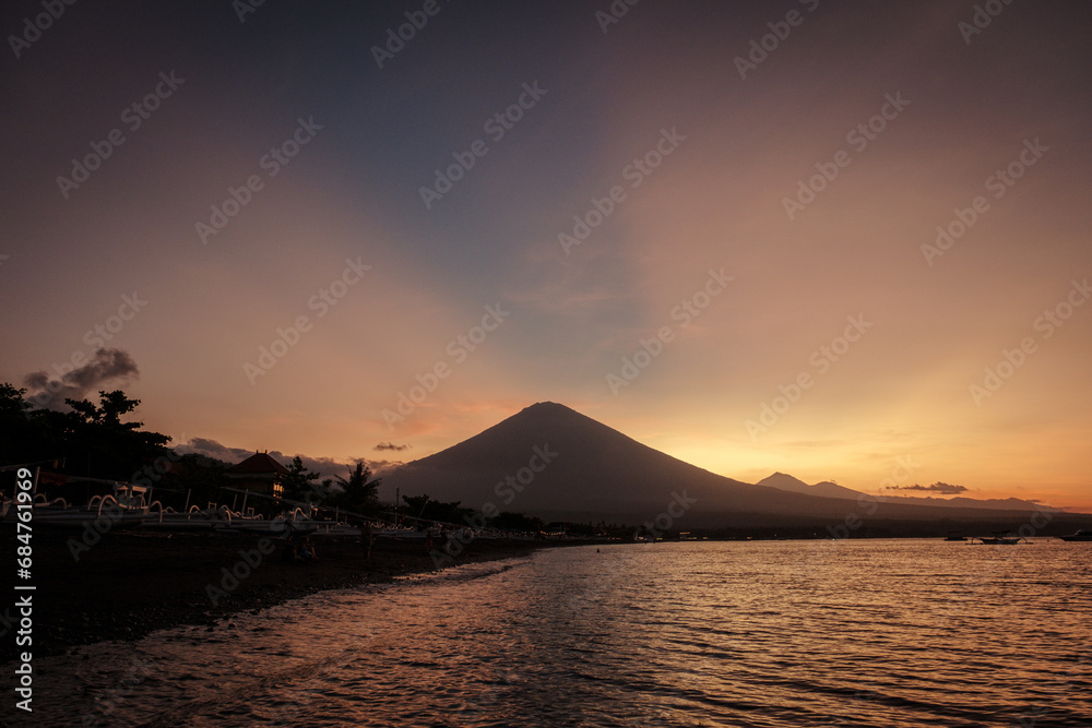 Sunset above Agung volcano from Amed with amazing sky. Black sand and traditional fishing boat.