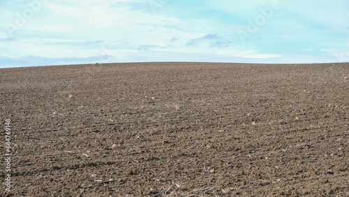 Ploughed farm field under a clear cloudy blue sky in an agricultural landscape. Open space area. 