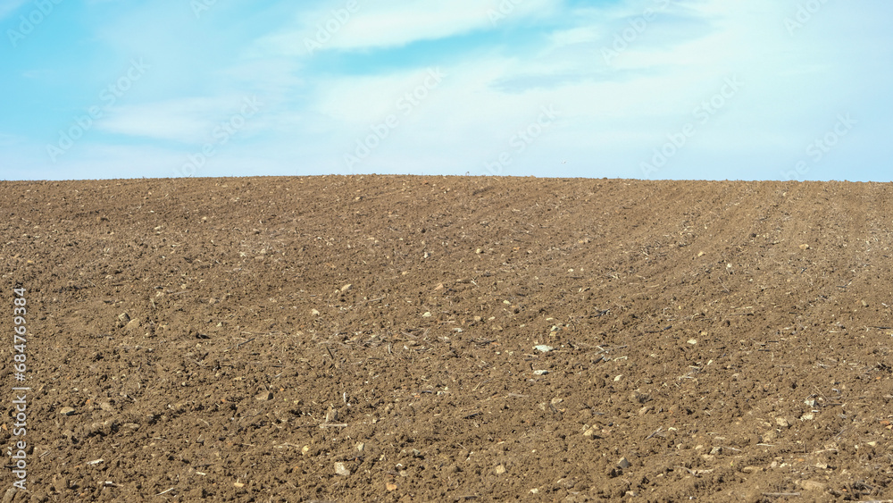 Ploughed farm field under a clear cloudy blue sky in an agricultural landscape. Open space area.
Ploughed farm field under a clear cloudy blue sky in an agricultural landscape. Open space area.