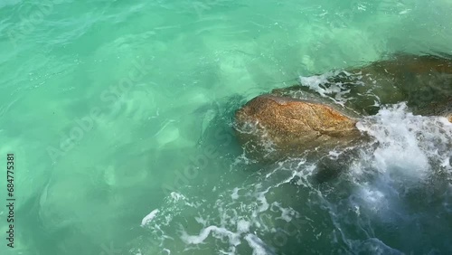 Sea waves with clear water crushing over the rocks during beautiful sunny day. 