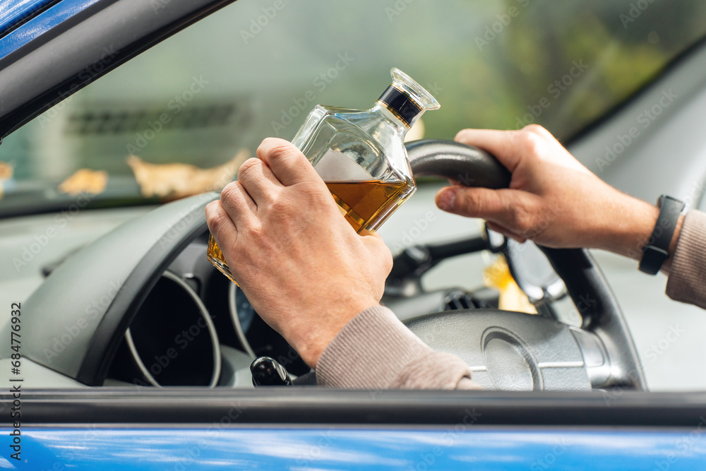 The driver is sitting behind the wheel and holding a bottle of alcoholic drink. Breaking the law and drinking alcohol while driving