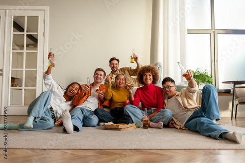 multiracial group of young people at house party eating pizza and drinking beer and having fun with friends
