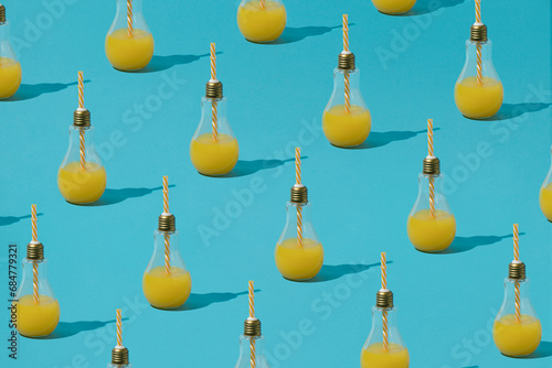 Foto Creative pattern made of light bulb glass with orange juice and straw against pastel blue background