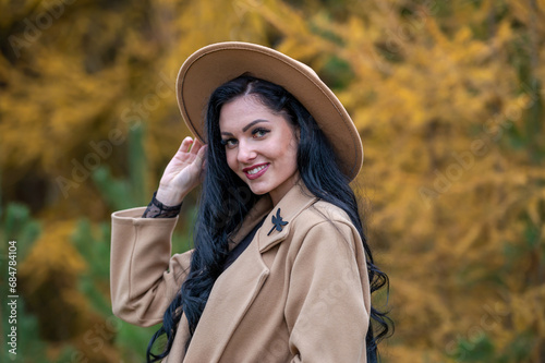 Beautiful brunette girl in beige coat and hat posing in autumn park
