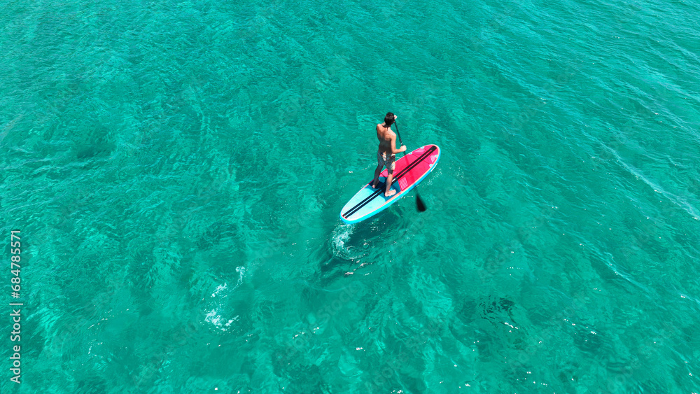 Aerial drone photo of fit man practise SUP or Stand Up Paddle board in tropical exotic bay with emerald calm sea