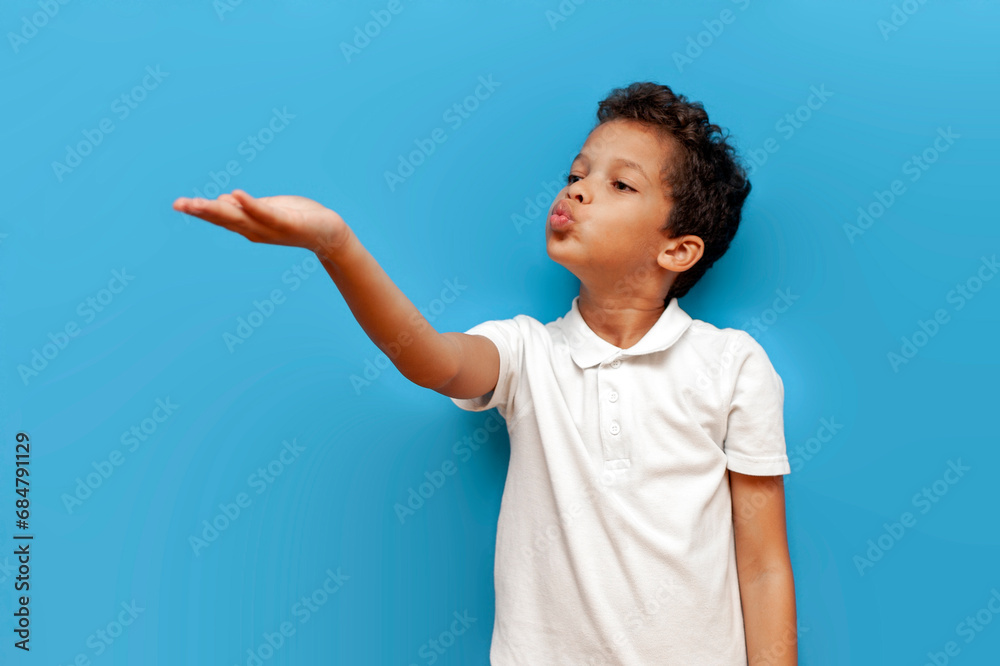 african american boy in white polo blows kiss on blue isolated background african american boy in white polo blows kiss on blue isolated background