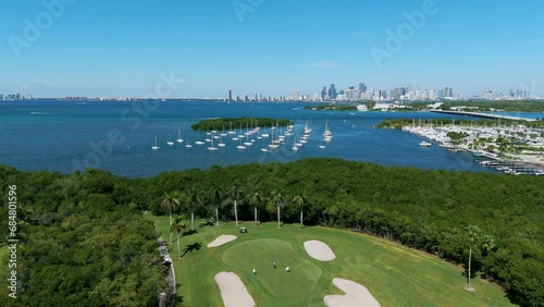Crandon Golf Course with players among lush tropical greenery of Key Biscayne island. Wonderful drone view on boats in marina, bridge and Brickell Downtown on background photo