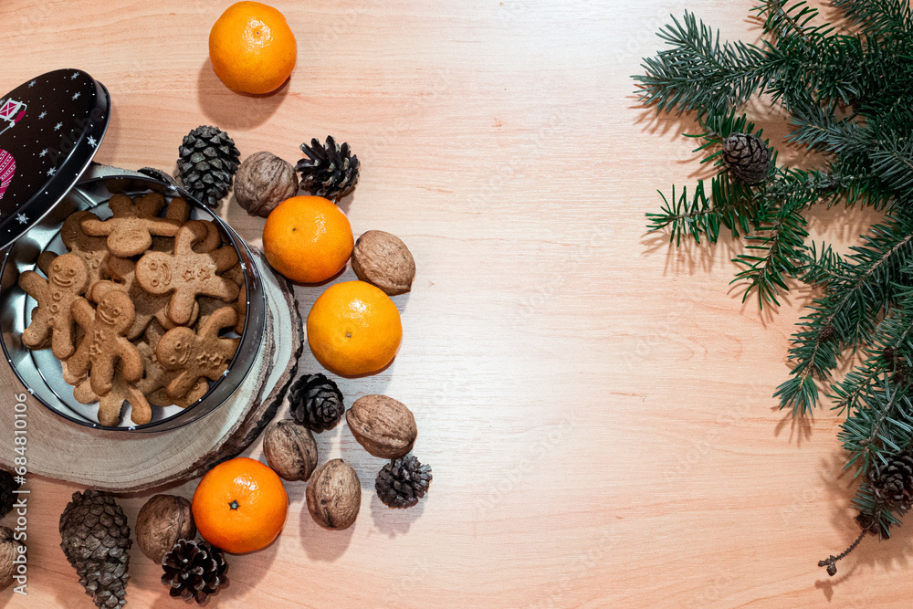Bird eye view on gingerbreads in a festive box on a wooden table adorned with seasonal accents of tangerines, pine cones, and walnuts contributing to the winter decor flavors and holiday traditions