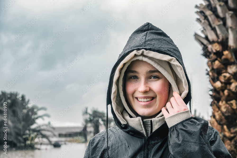 Portrait of a smiling young woman in a raincoat during a storm, hurricane, downpour on the island against the backdrop of the sea