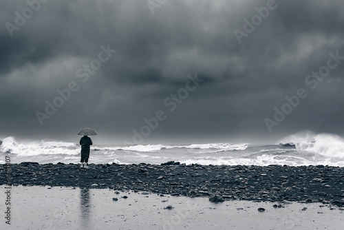 man on the shore near the sea  ocean in a raincoat and with an umbrella during a storm  hurricane  downpour. Natural disasters  apocalypse