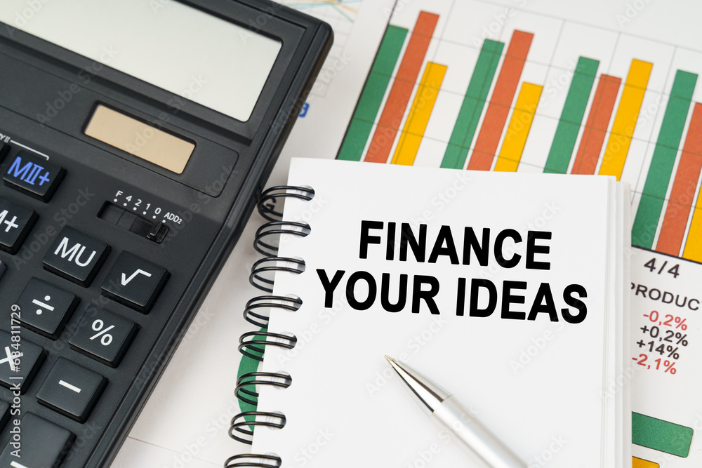 On business charts there is a calculator, a pen and a notepad with the inscription - FINANCE YOUR IDEAS On business charts there is a calculator, a pen and a notepad with the inscription - FINANCE YOUR IDEAS