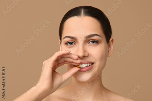 Pretty young woman taking vitamin A capsule on beige background, closeup