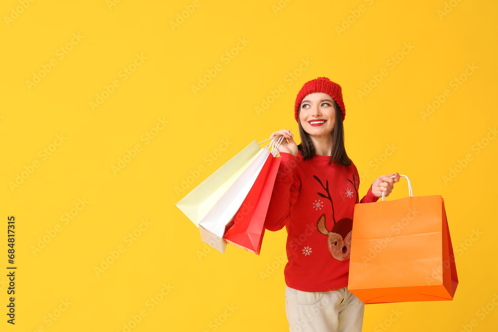 Young woman holding shopping bags on yellow background