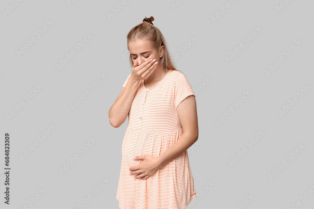 Beautiful young pregnant woman suffering from toxicosis on grey background Beautiful young pregnant woman suffering from toxicosis on grey background