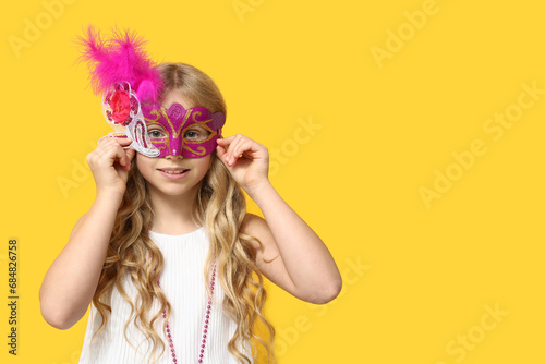 Adorable little girl wearing carnival mask on yellow background photo